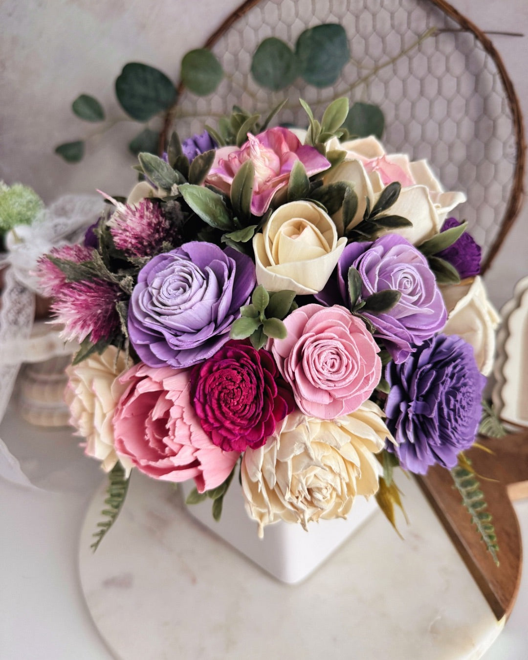 Colorful flower arrangement with roses and thistles in a white vase on a marble surface.