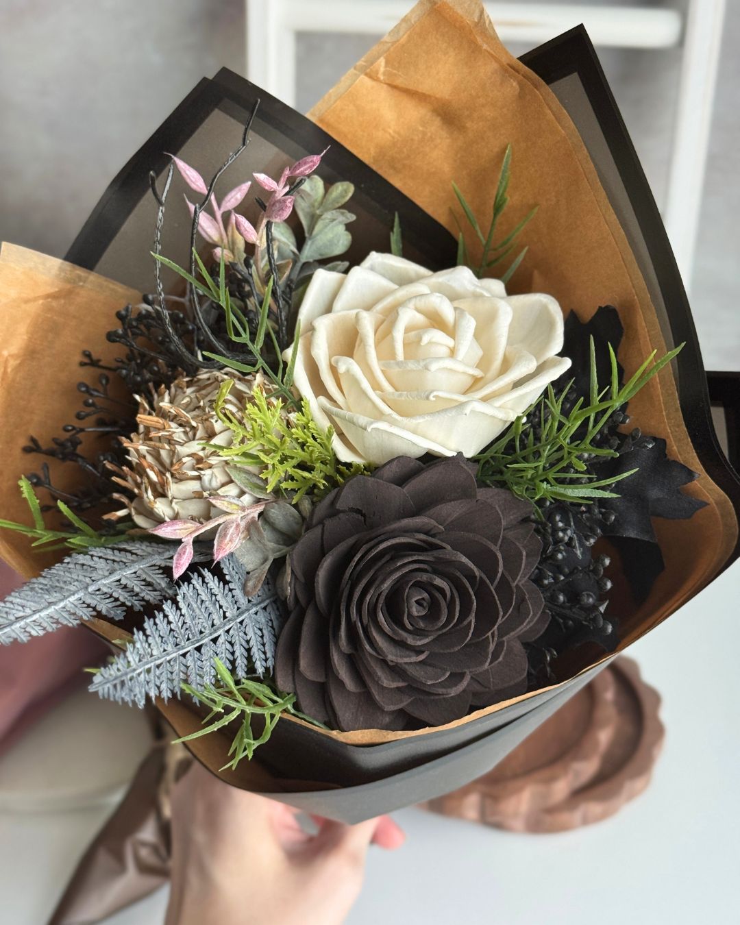 Bouquet of flowers wrapped in brown paper with a black box, held by a hand.