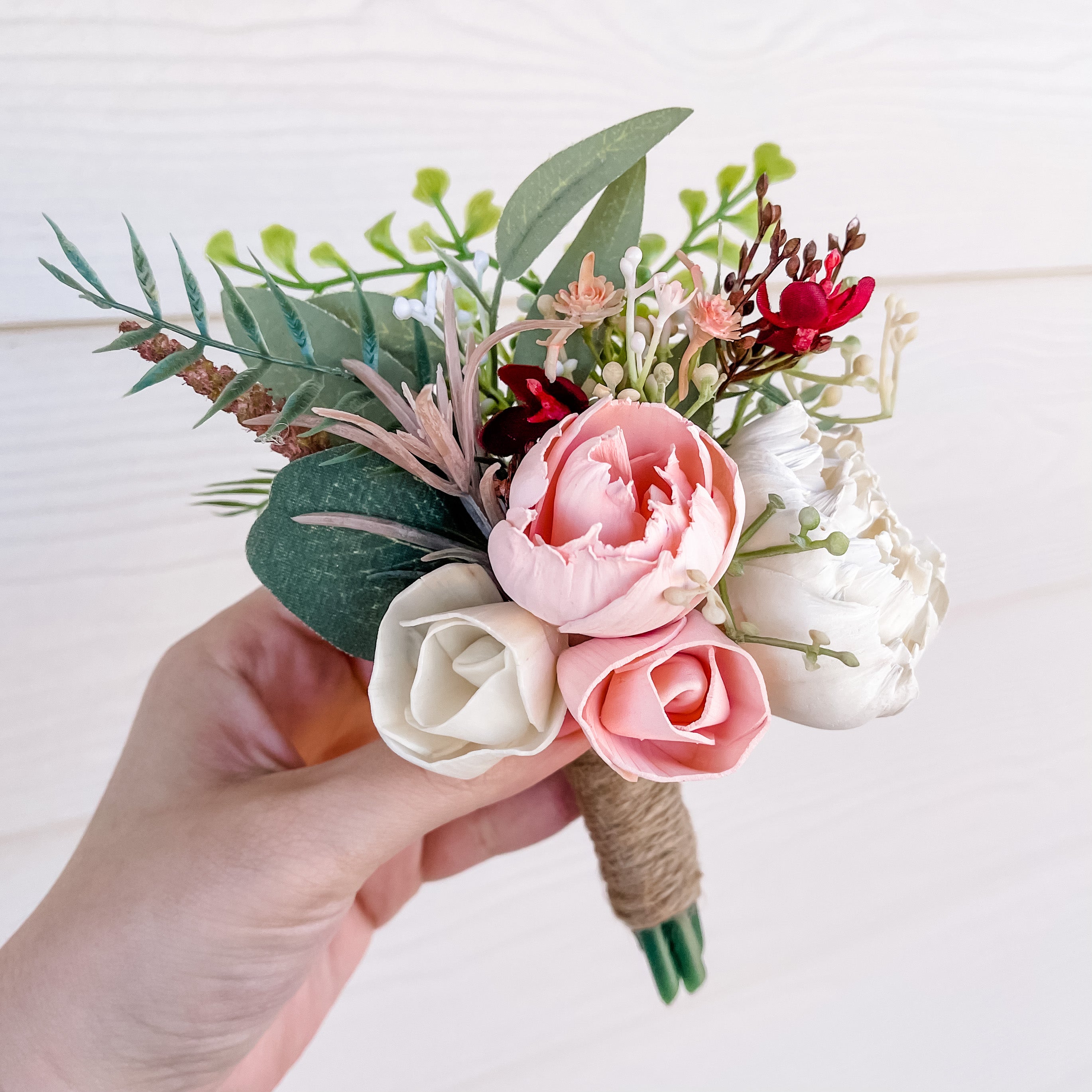 Hand holding a small bouquet of flowers with pink, white, and red roses on a light background