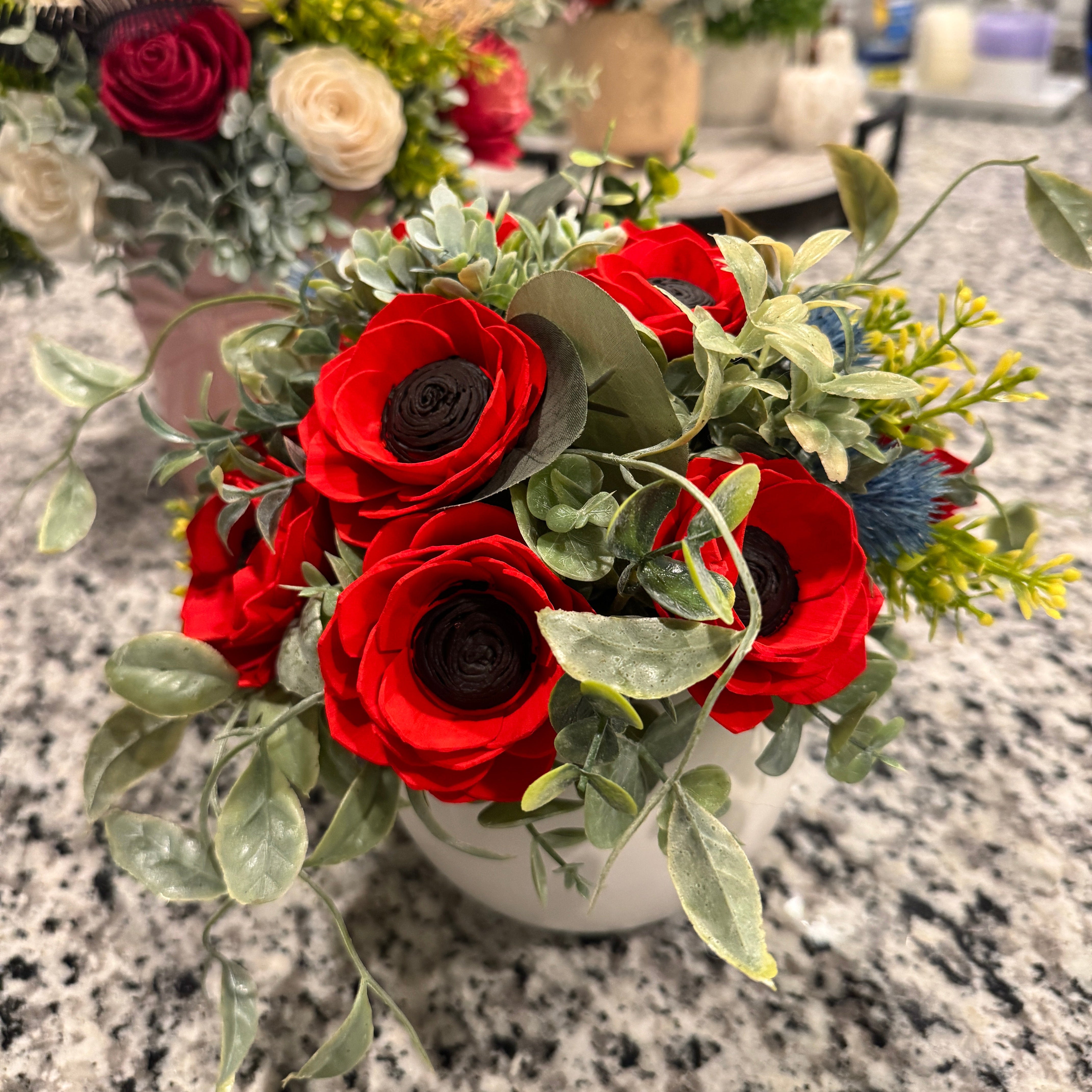 Bouquet of red and green flowers on a marble countertop with other floral arrangements in the background.