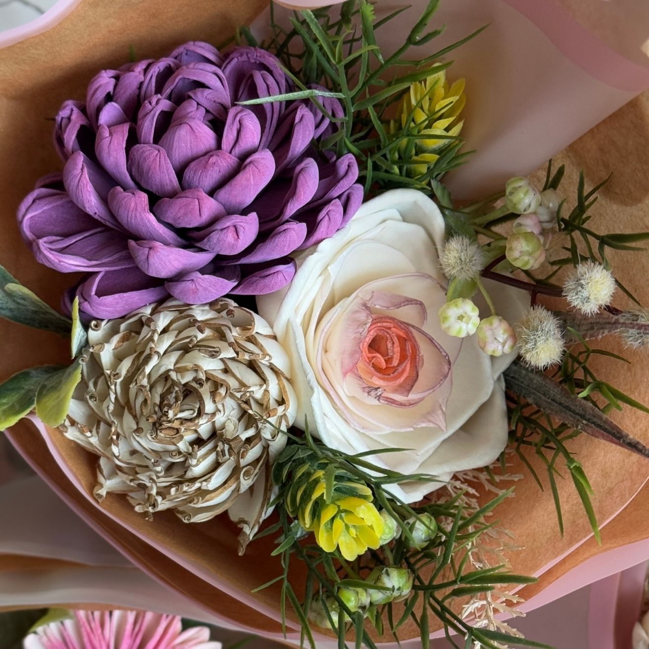 Bouquet of flowers with a purple flower, white rose, and greenery on pink paper.