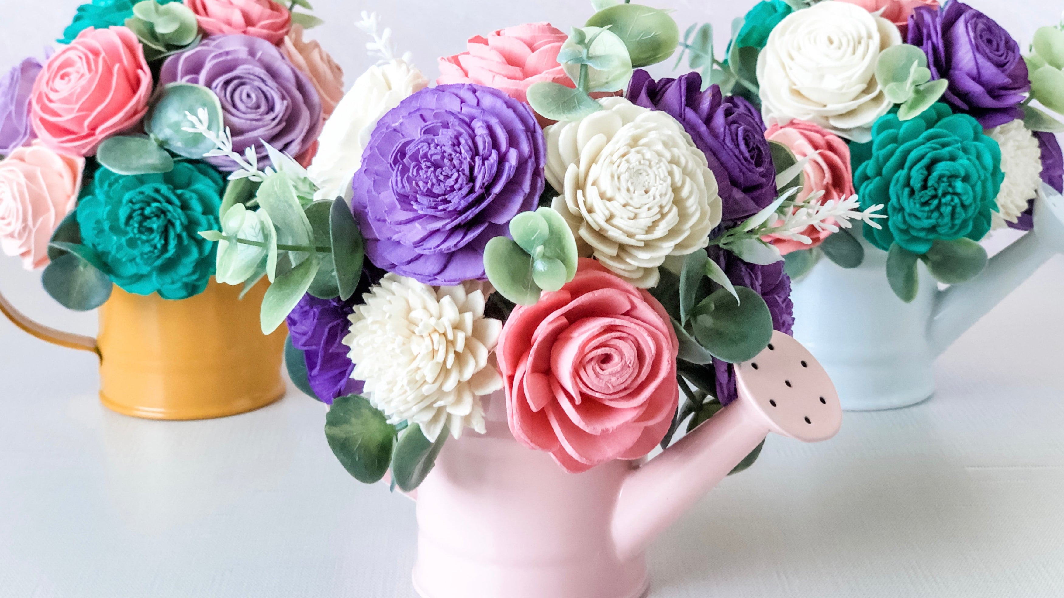 Colorful flower arrangements in small watering can-shaped vases on a white background