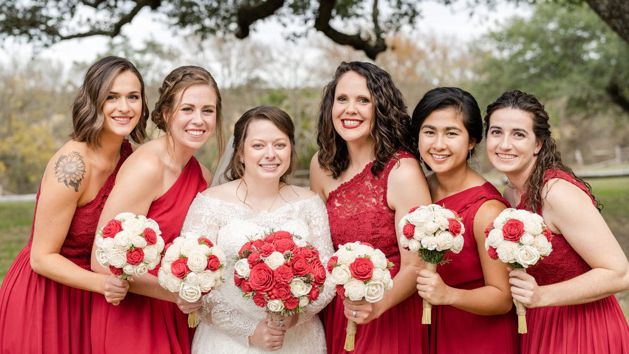Bride and bridesmaids in red dresses with floral bouquets outdoors.