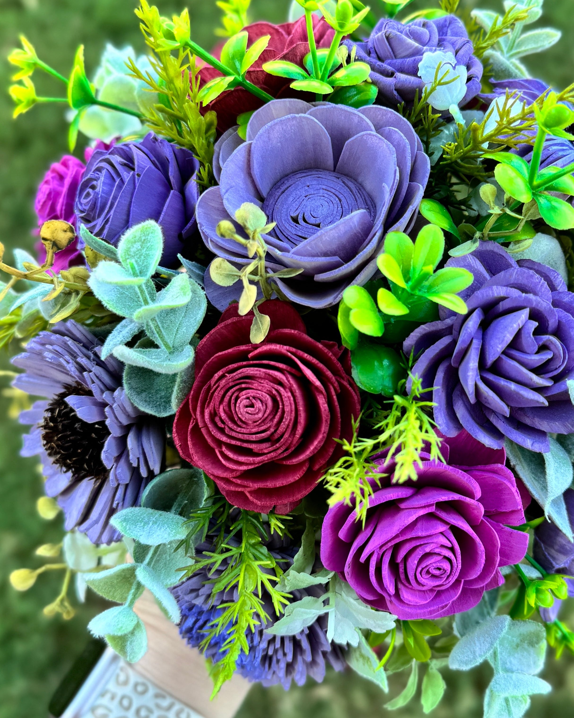 Bouquet of purple and red artificial flowers with green leaves held by a person.