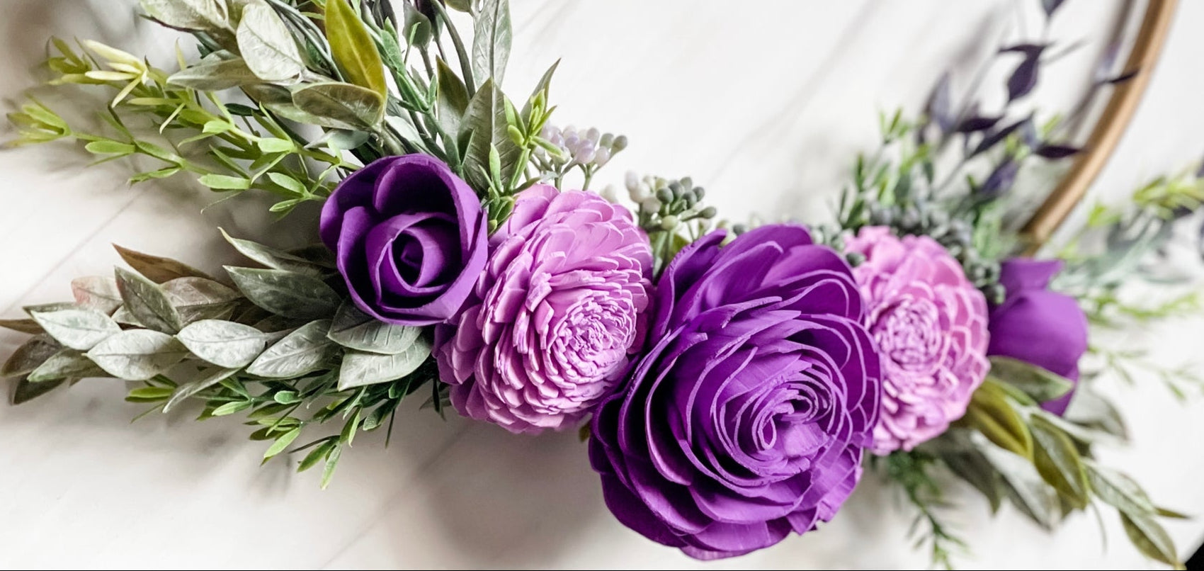 purple wood flowers on a gold hoop with faux greenery attached