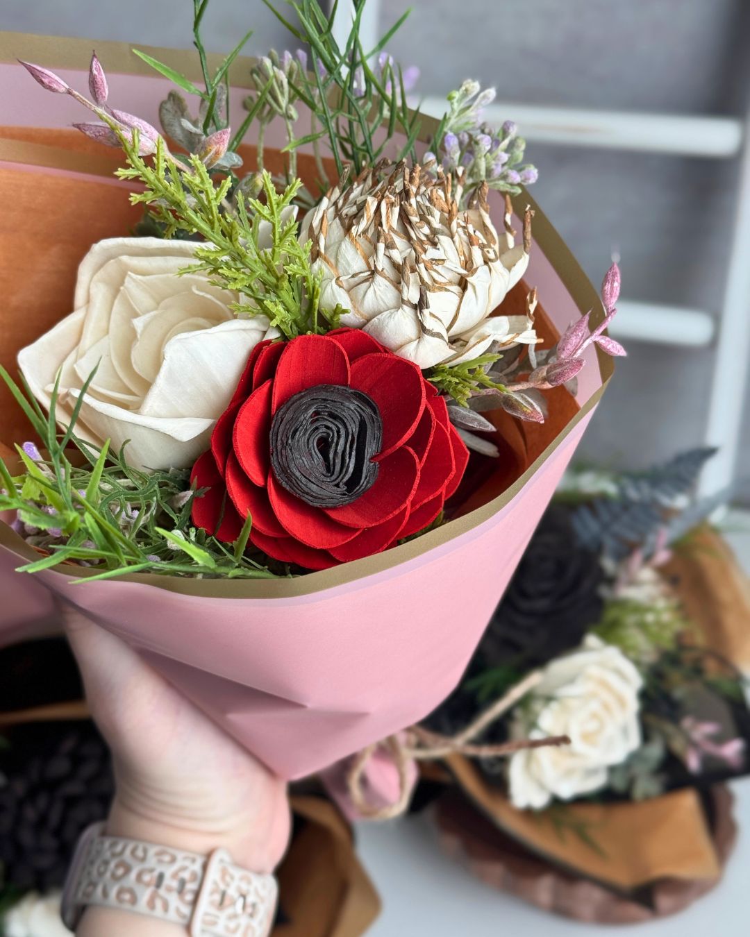 Bouquet of artificial flowers in a pink holder held by a hand.