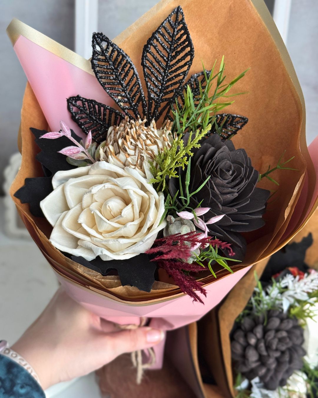 Bouquet of decorative flowers with black, white, and green leaves held by a hand.
