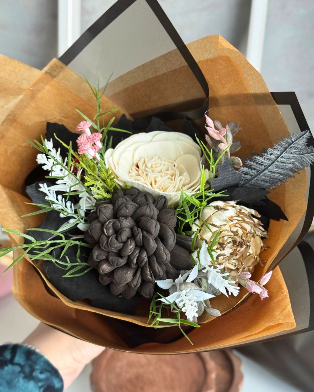 Bouquet of flowers with black and white elements wrapped in brown paper.