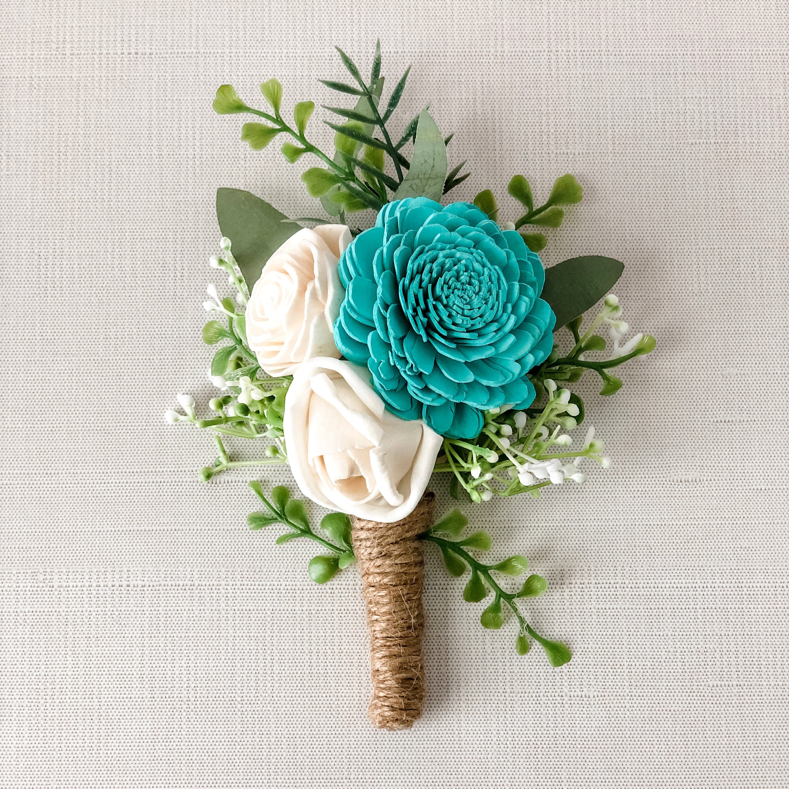 Teal and white floral boutonniere with greenery on a light gray background