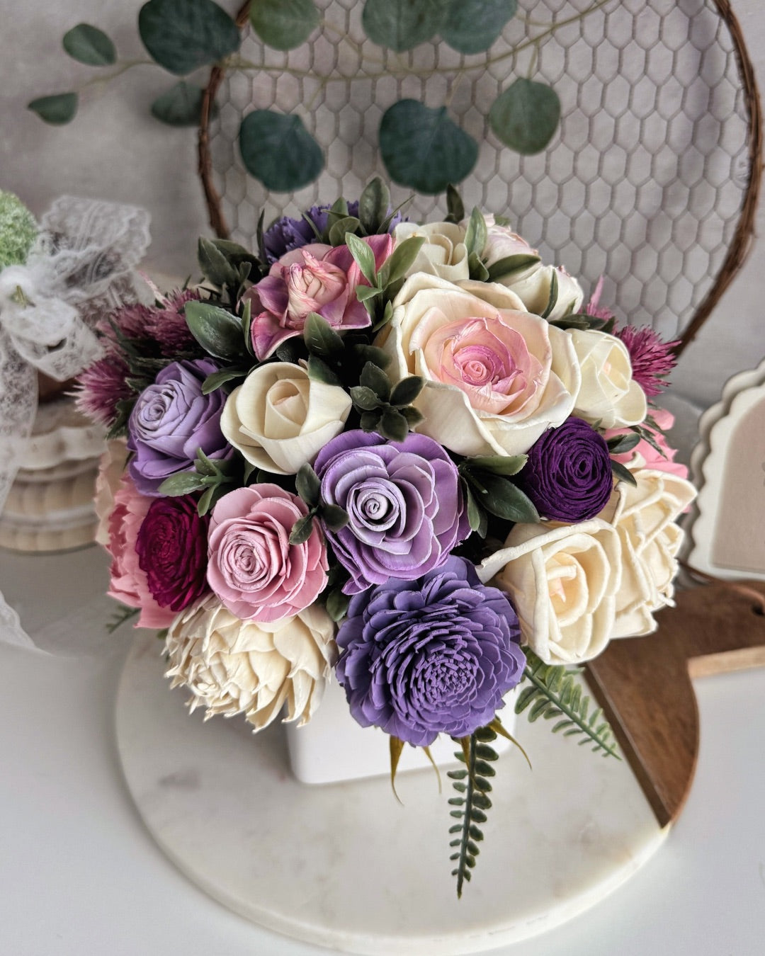 Bouquet of pink, purple, and white roses on a decorative stand with greenery.