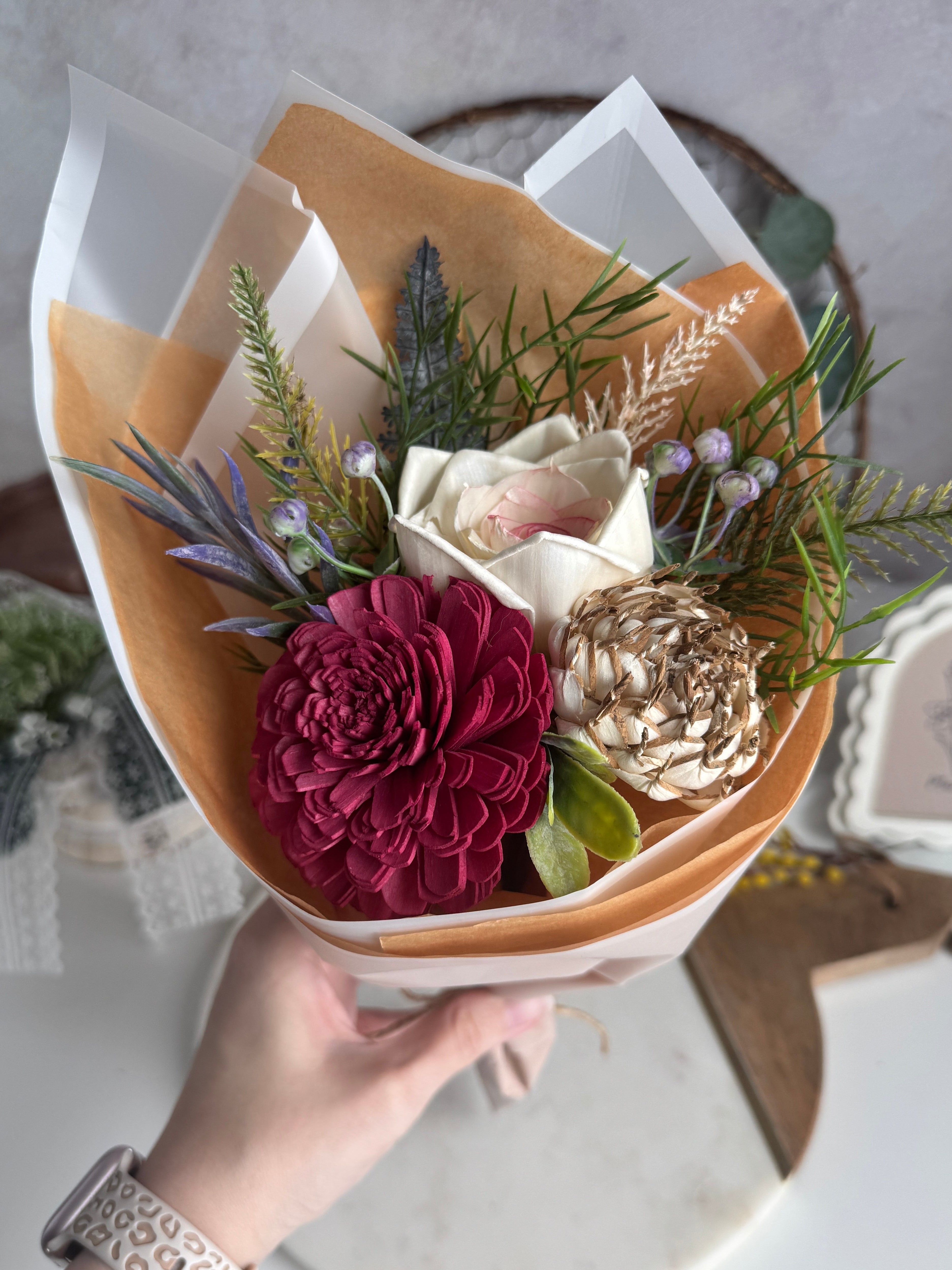 Bouquet of flowers wrapped in brown paper held by a hand on a light background