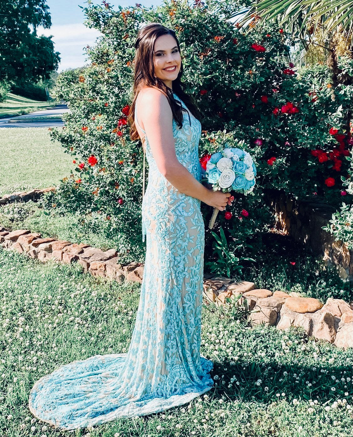 Woman in a light blue lace dress holding a bouquet of flowers, standing in a garden.