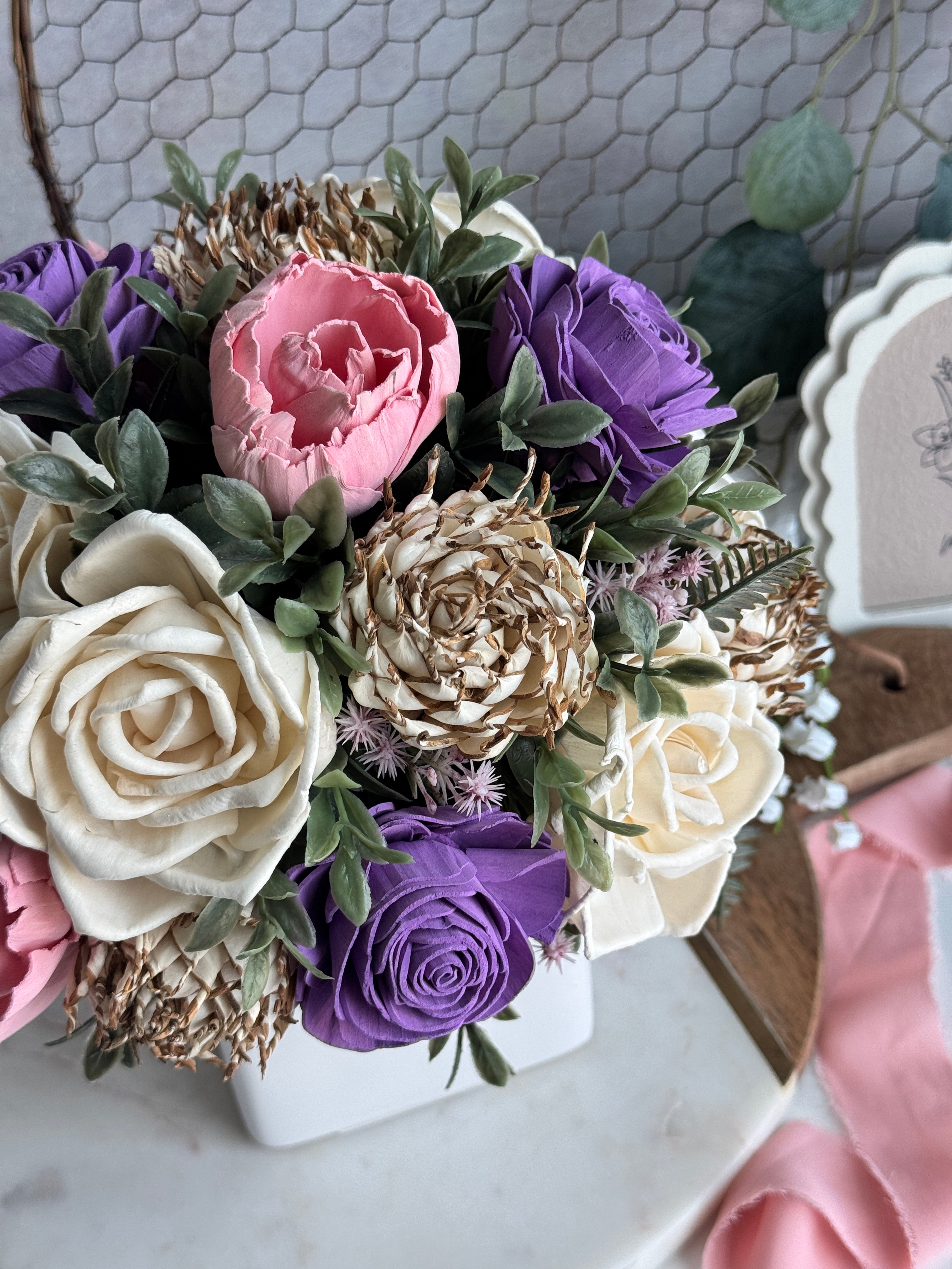Bouquet of artificial flowers including purple, pink, and white roses on a marble surface.