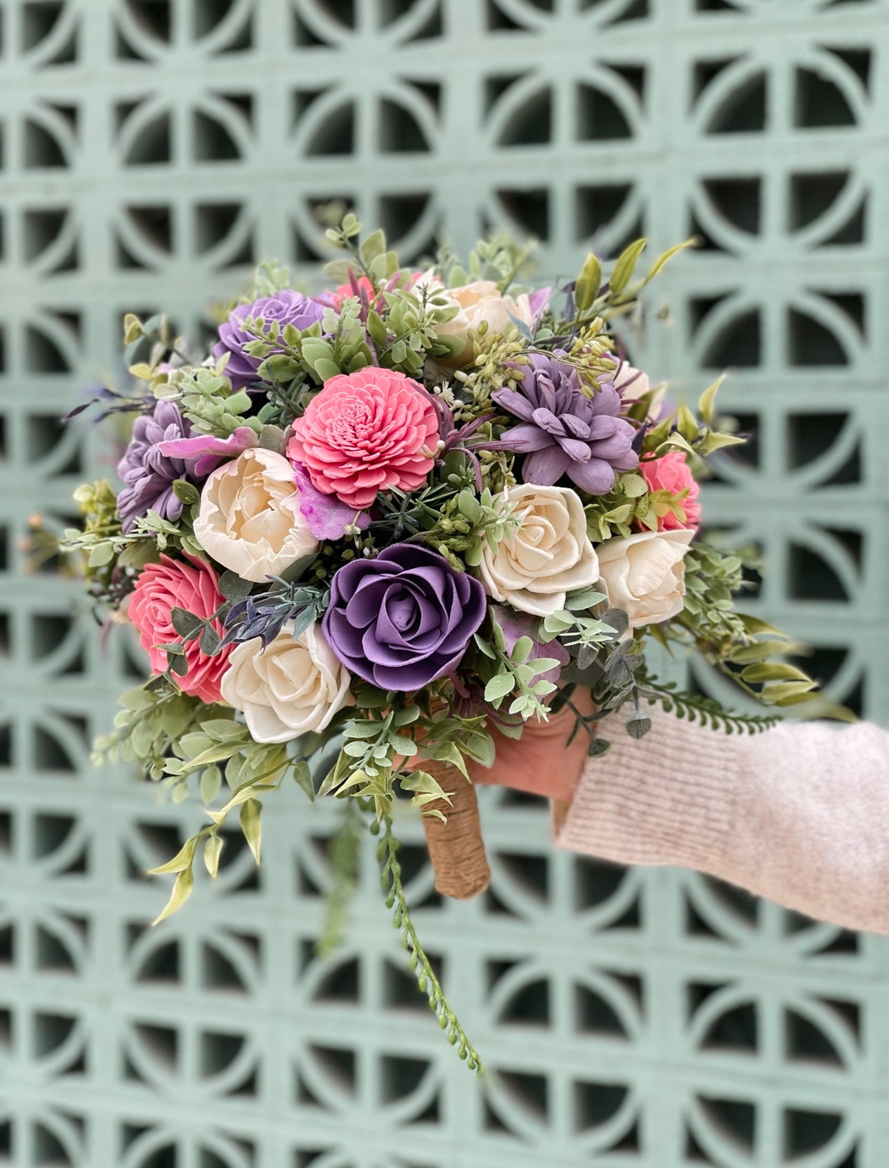 Bouquet of artificial flowers held by a hand against a patterned wall.