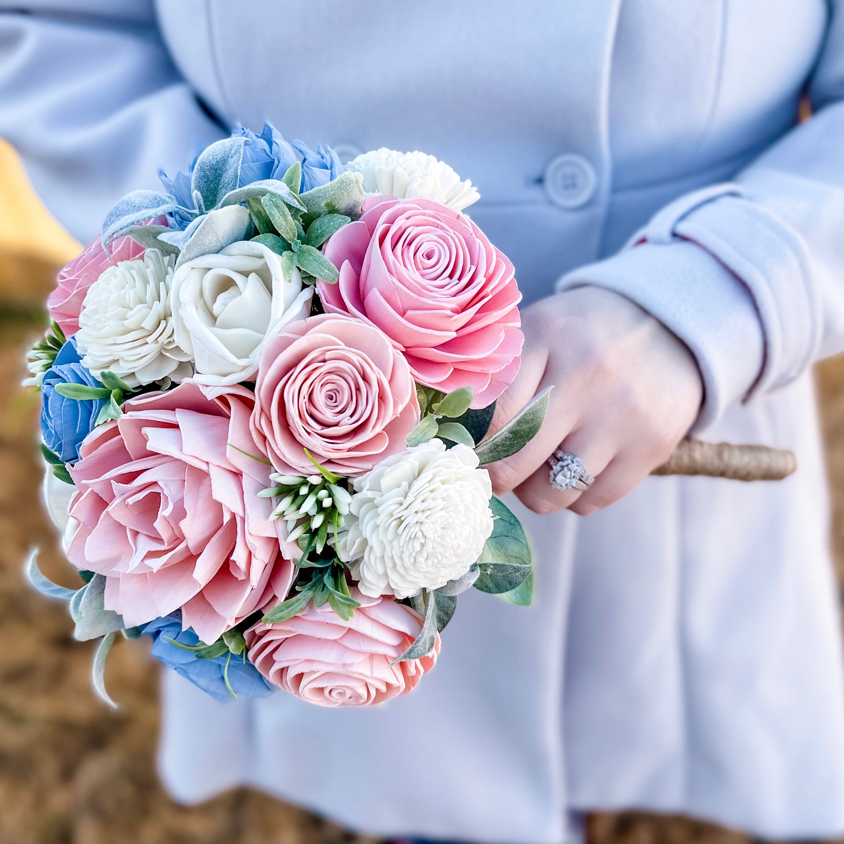 Bouquet of pink, white, and blue flowers held by a person wearing a light blue coat.