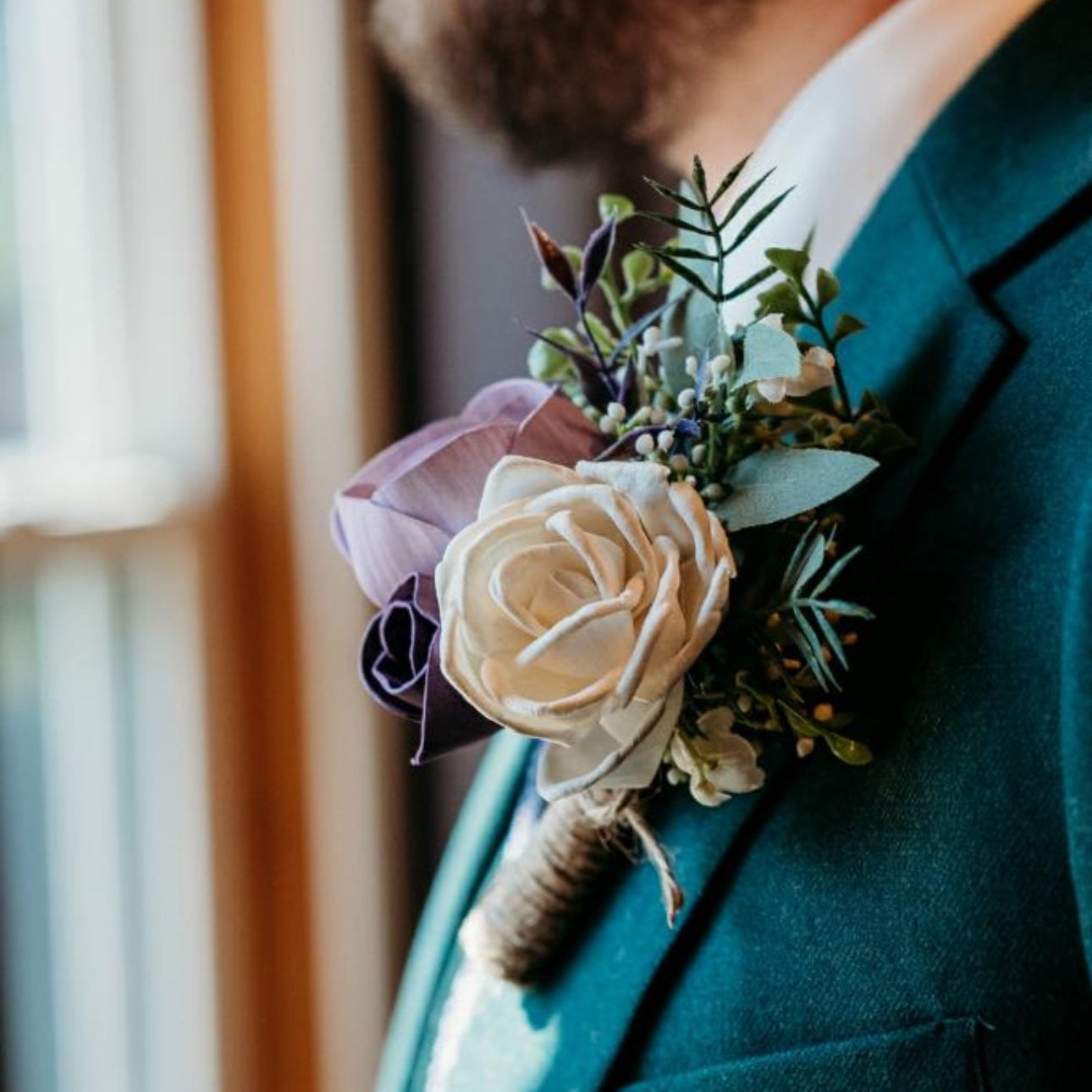 Man wearing a teal suit with a floral boutonniere against a blurred indoor background
